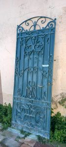 old iron door with spirals and twirls and an oval arch on the top part, solid iron in blue color, heavy external barred door, garden door, iron garden gate, heavily built, handmade