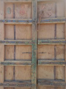 pair of old wooden doors , natural wood color, with green details, and iron blades decorated with iron rosettes
