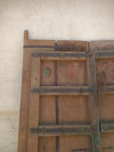 pair of old wooden doors , natural wood color, with green details, and iron blades decorated with iron rosettes